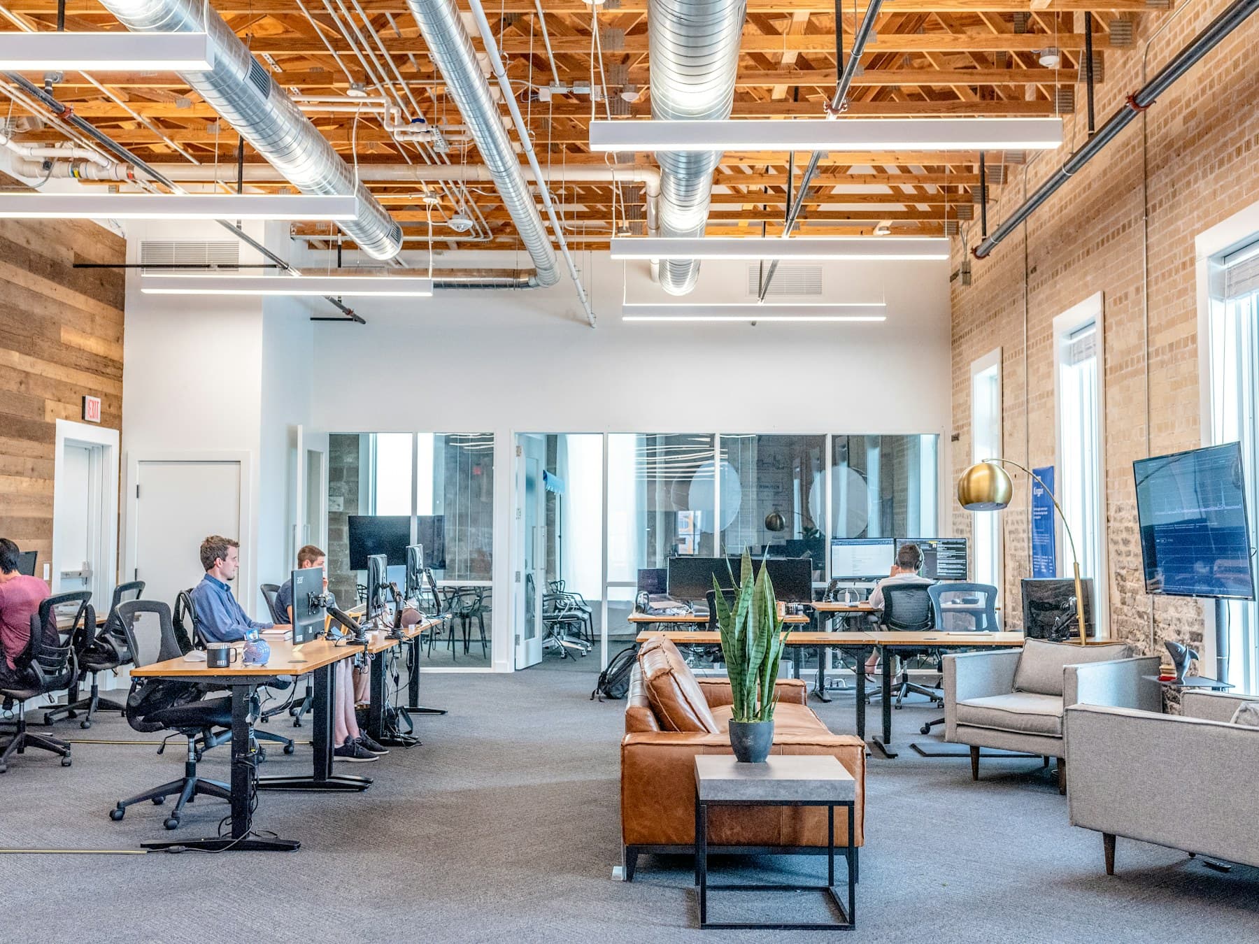 People working at desks in a bright loft office with wood and brick